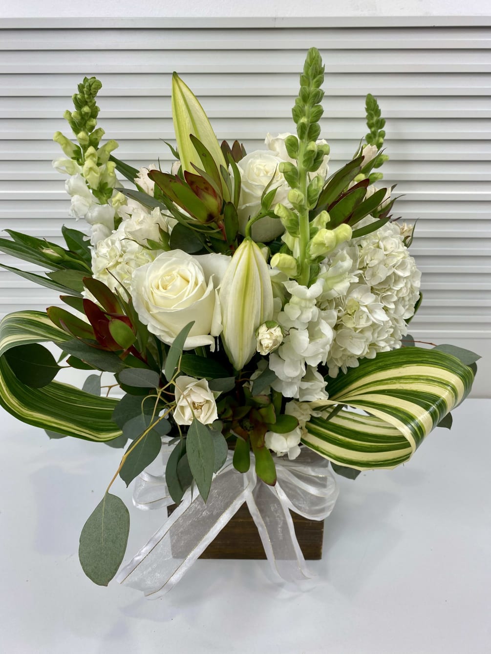 Green and white arrangement in a wooden vase. Hydrangeas, snapdragon, roses and