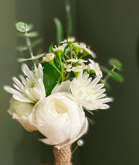 Boutonniere with a white ranunculus at the center surrounded by white mums