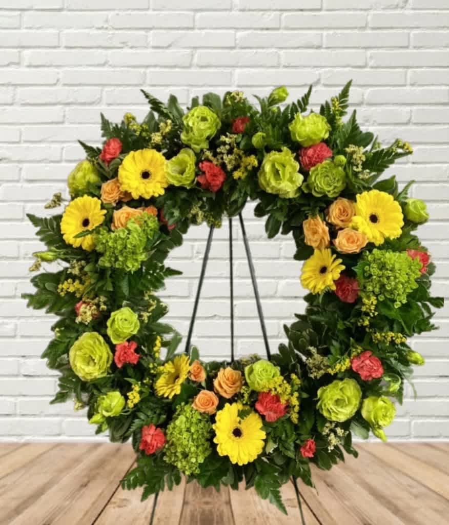 A wreath display on an easel mixed with radiantly bright flowers. 
