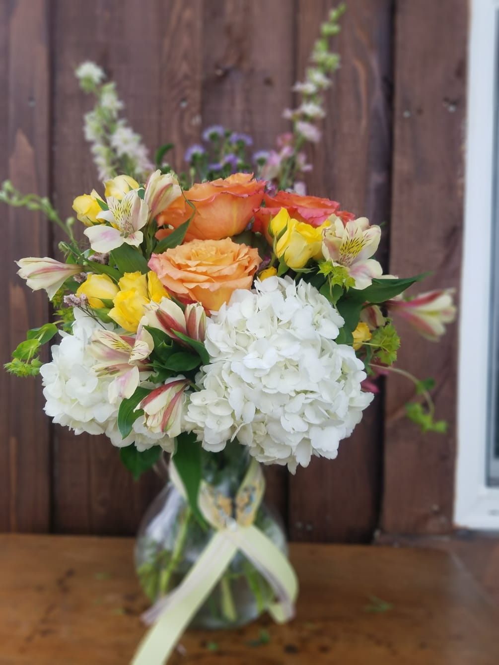 An elegant vase filled with roses, hydrangeas, larkspur, alstromeria, spray roses and