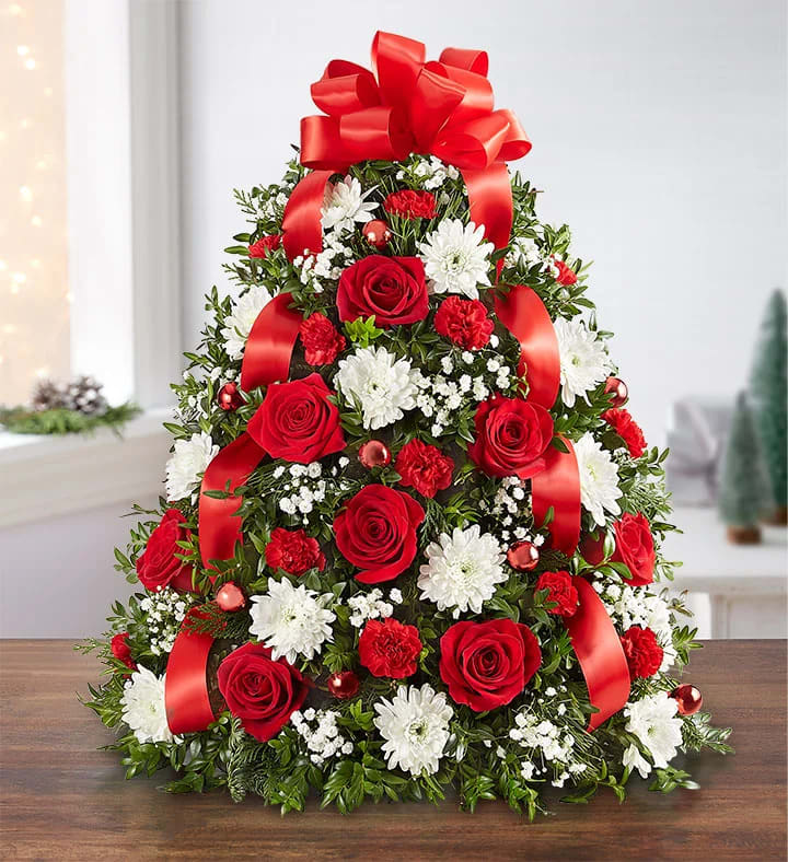 A tree-shaped arrangement with red roses and mini carnations. White cushion; accented