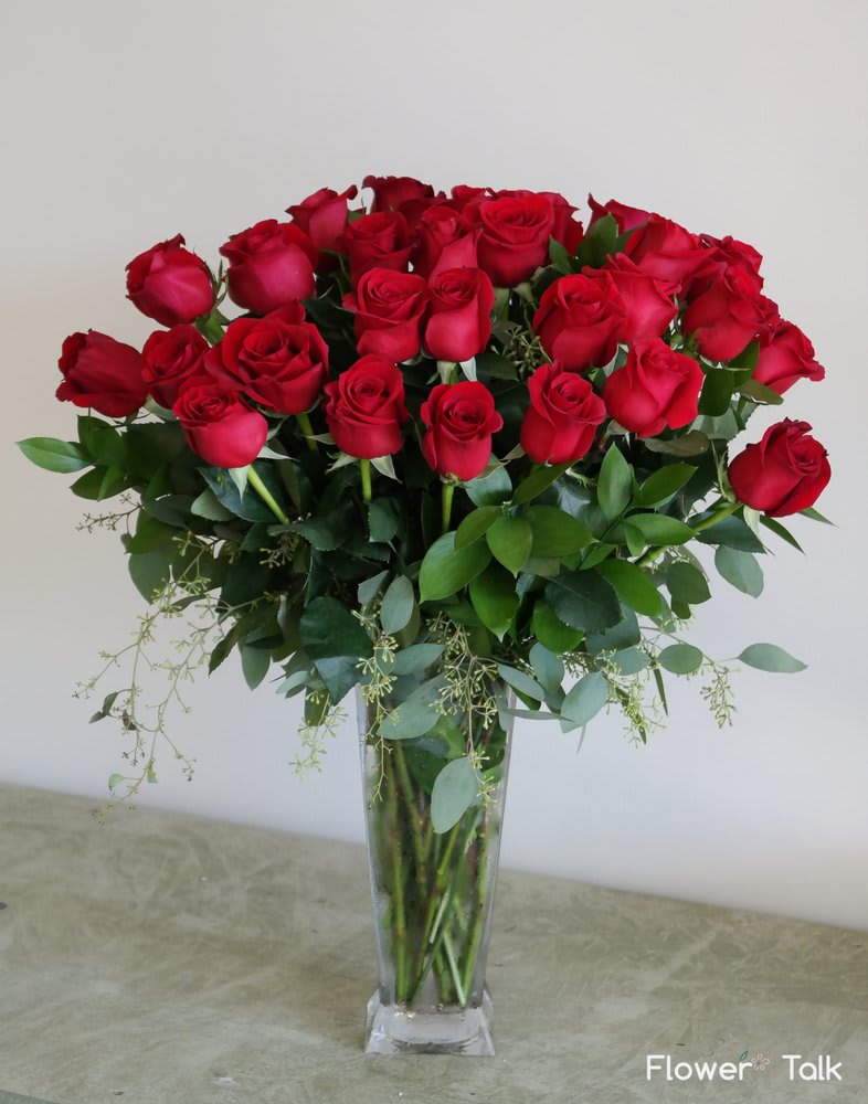 Vibrant red roses arranged with seeded eucalyptus in a tall glass vase.