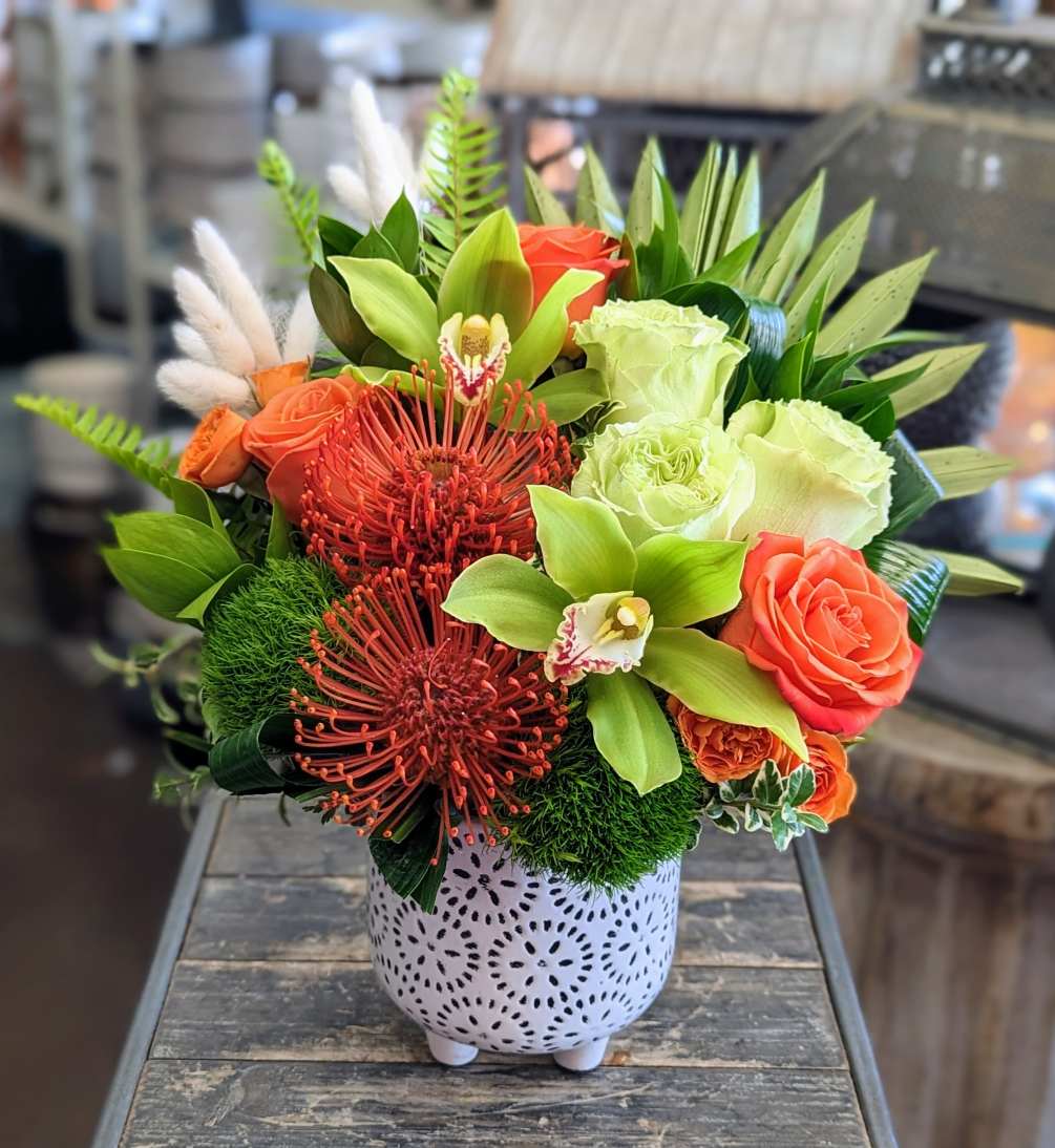 A mix of roses, pincushion protea, orchids, and mixed greenery in a
