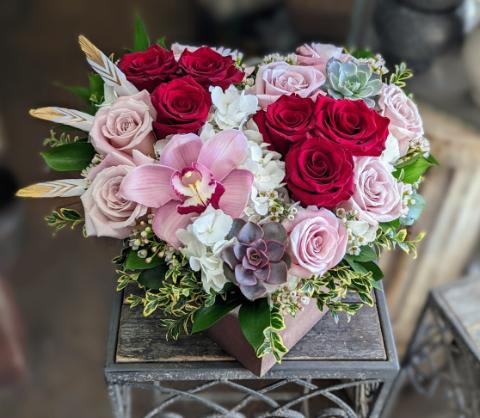 A heart-shaped wooden box with hydrangea, red and pink roses, a cymbidium