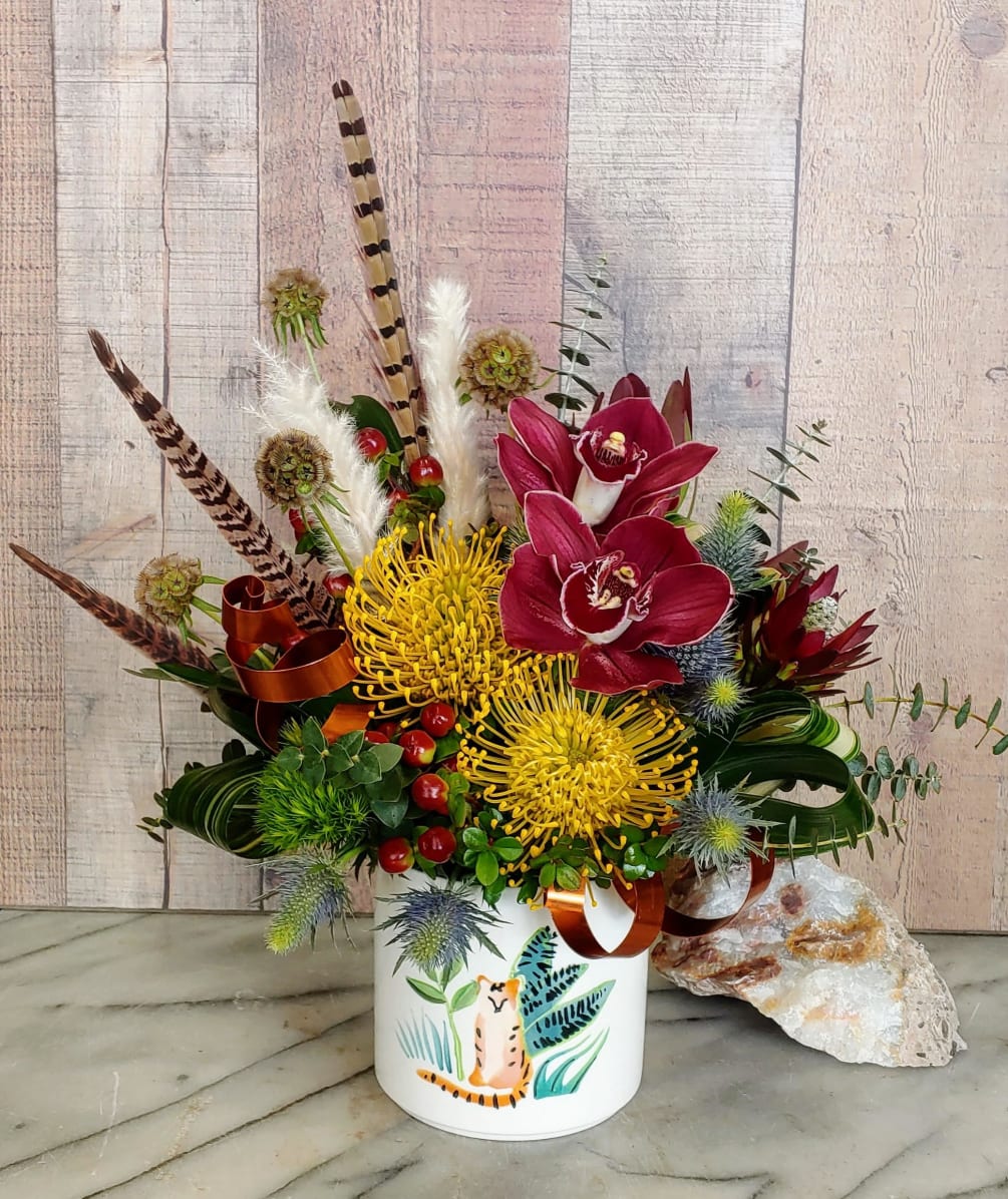 Protea, orchids, and assorted greenery in a keepsake container.
