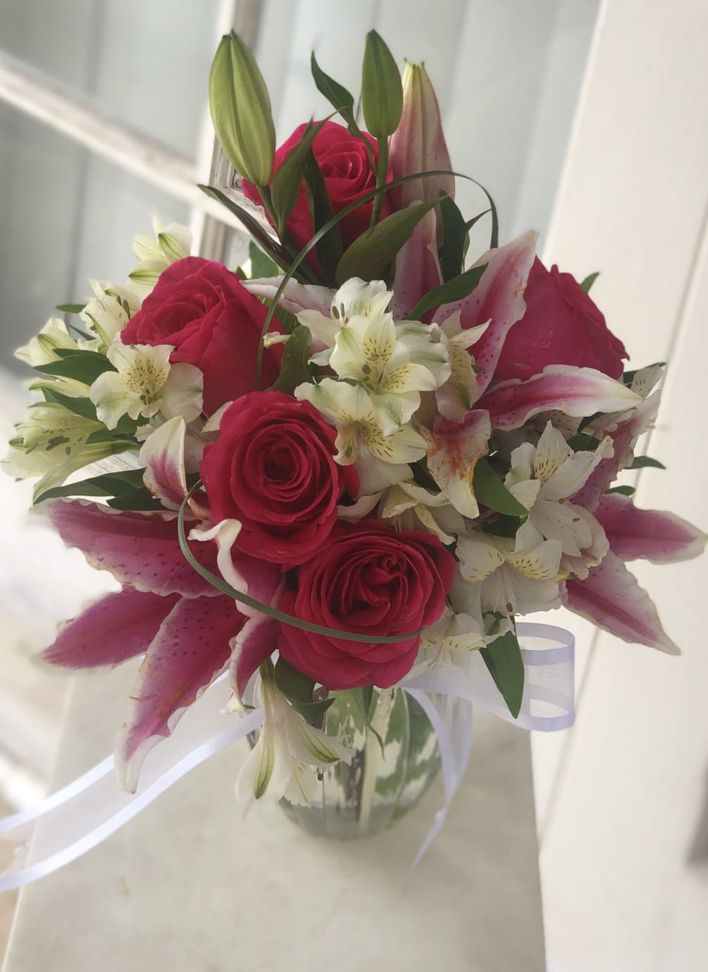 Hot pink roses, stargazer lilies, accented with other blooms  are arranged