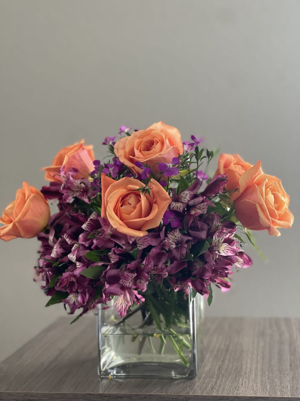 Lovely floral arrangement of orange roses, purple alstroemeria flowers and purple dianthus
