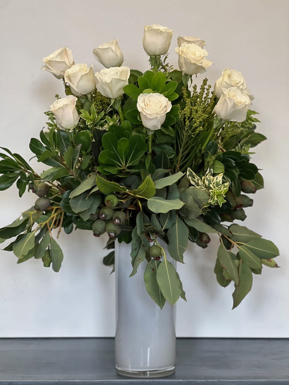 A dozen roses accentuated by textures of lush greenery.  If you