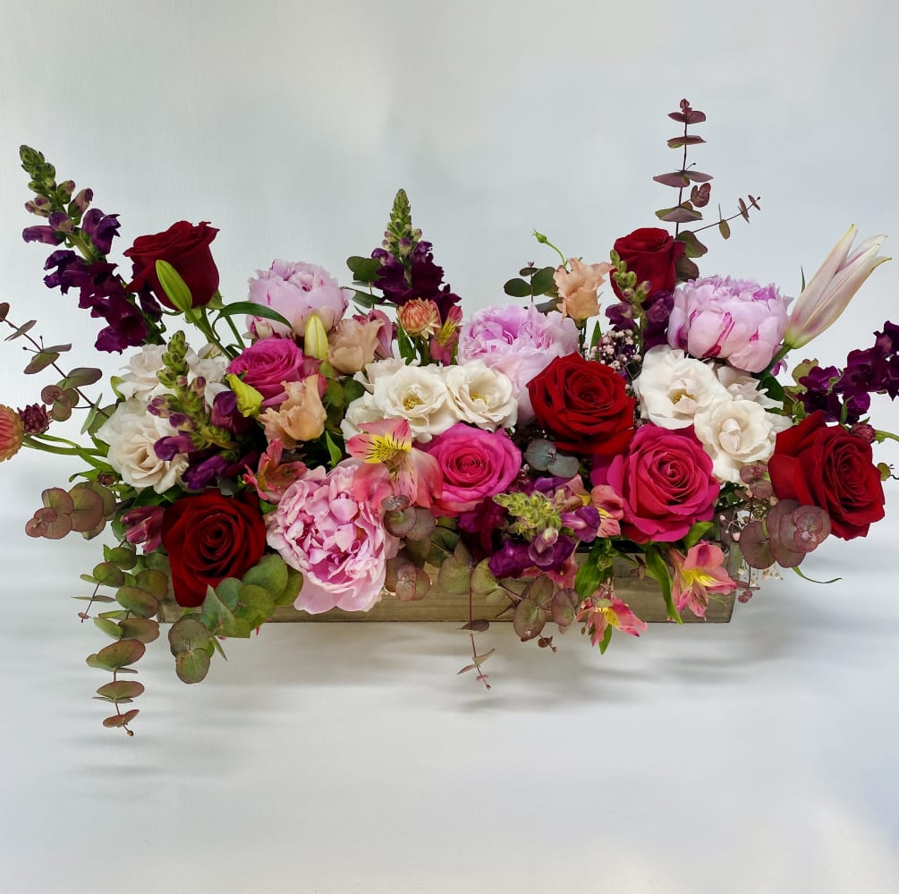 Long wooden tray full of elegant and romantic peonies, roses, ranunculus, snapdragons