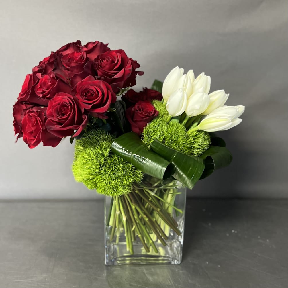 Roses and tulips are arranged together in a glass block vase. 