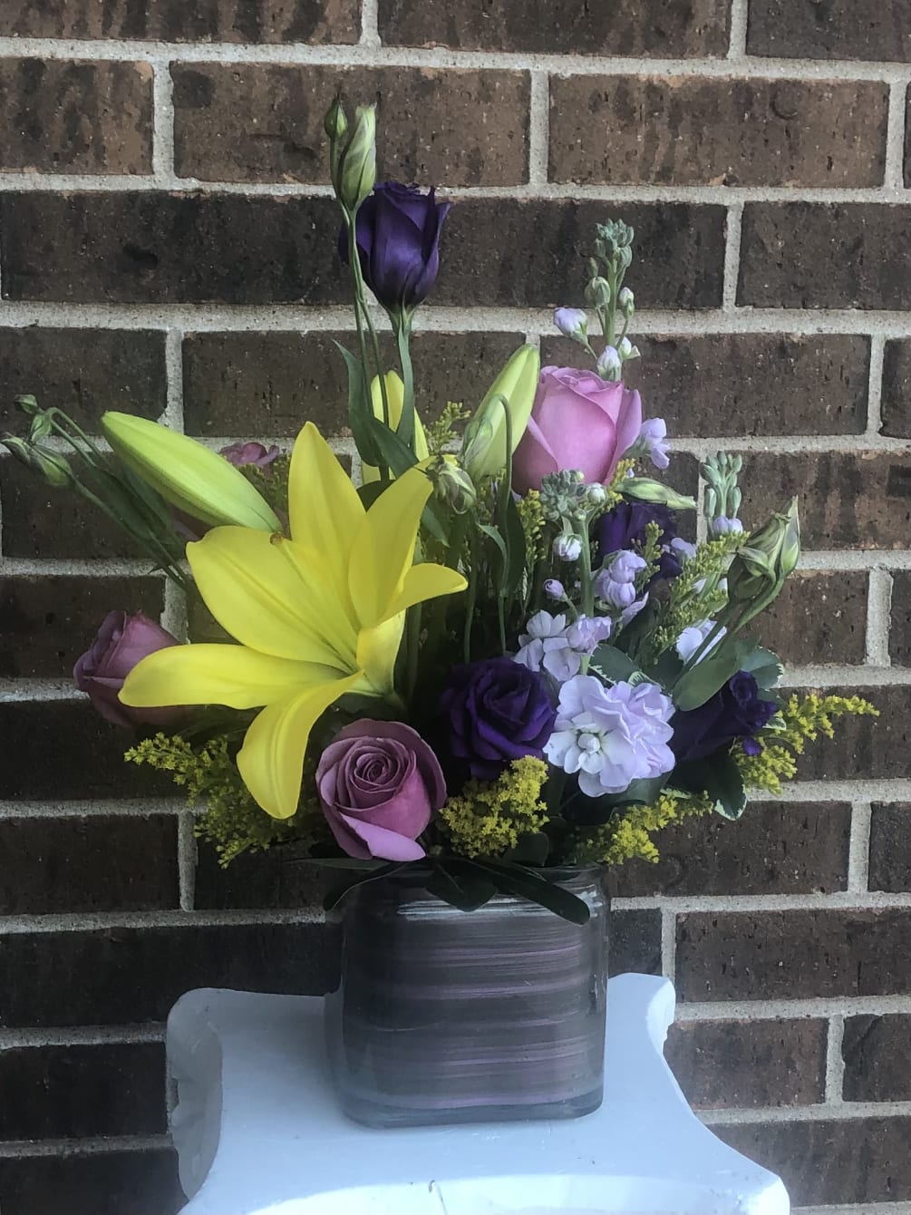 Yellow lily, lavender roses and stock, lisianthus and solidago in a vase.