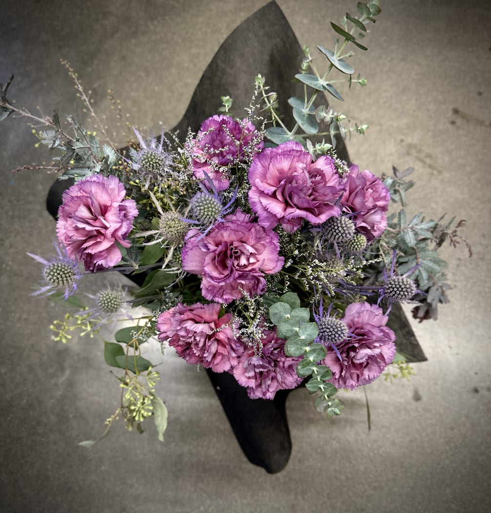 A gift wrapped bouquet of carnations mixed with textural flowers and foliage.