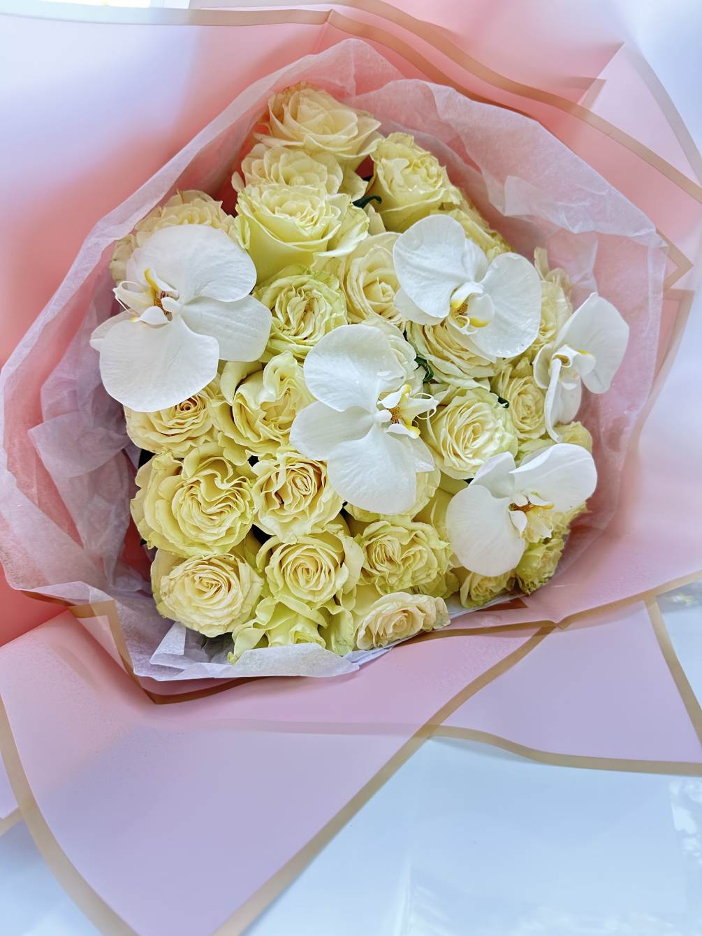White Mondial roses united with orchids in a beautiful hand tied bouquet