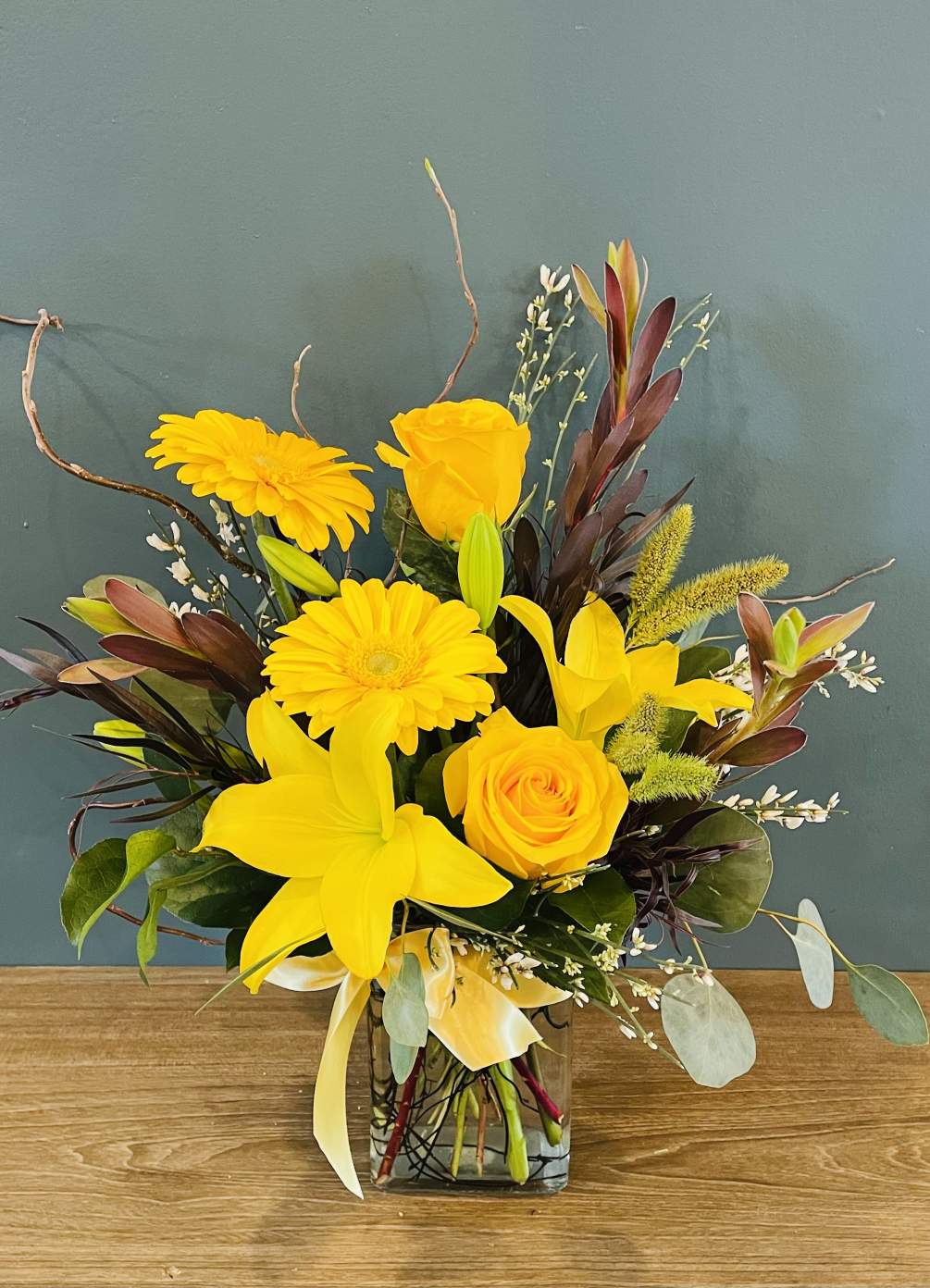 A bright yellow bouquet of gerbera daisies, roses, lilies and leucadendron accented