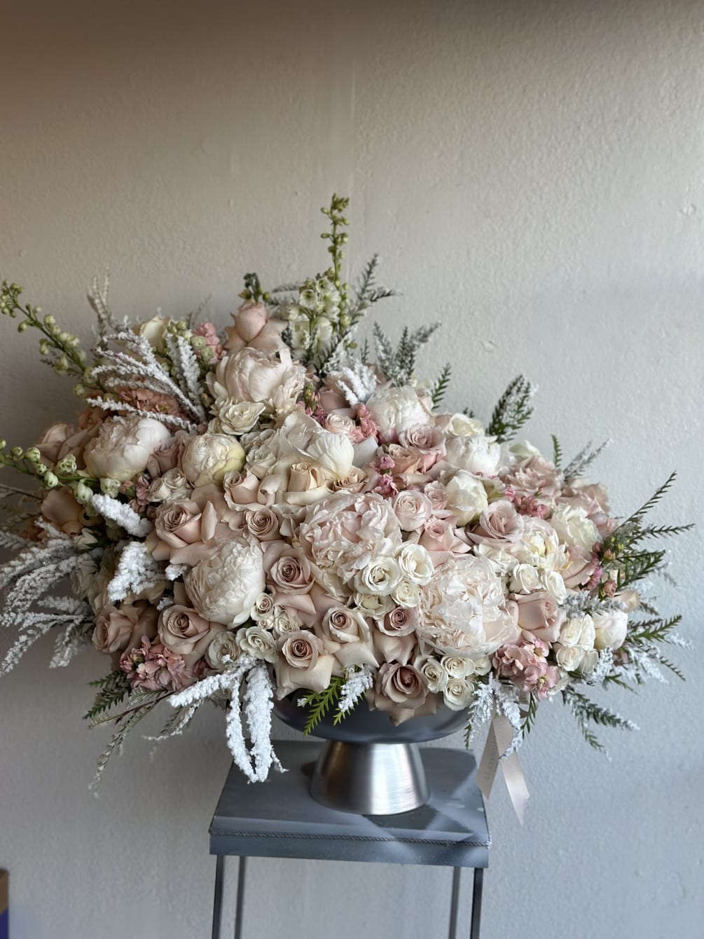 Silver vase filled with white and nuderoses, white peonies, and winter greenery.