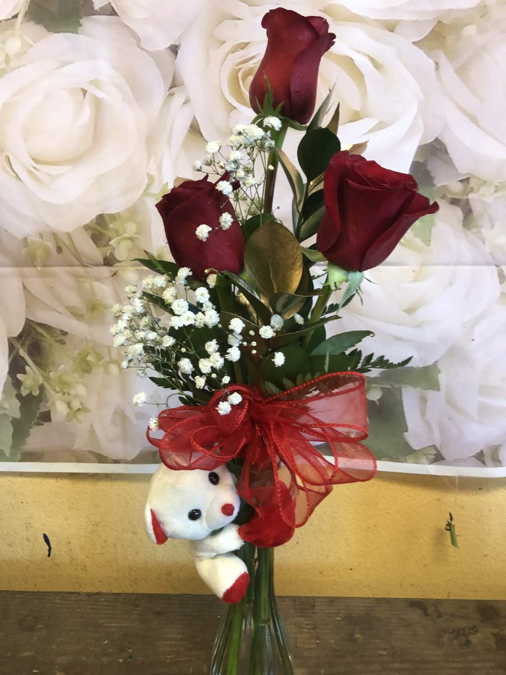 3 Roses in a vase and a bear is hugging the vase