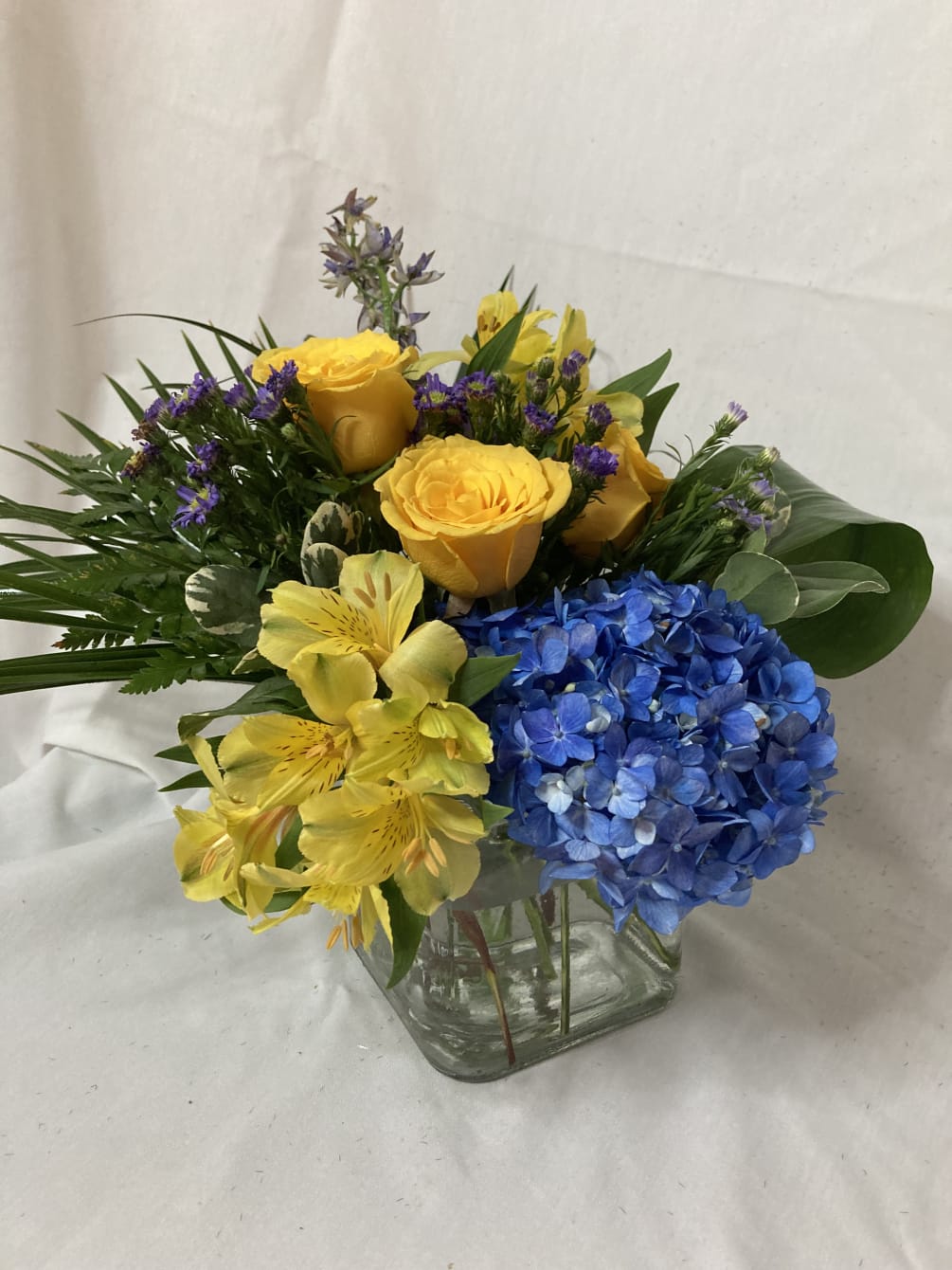 Lovely blue hydrangea, yellow roses, yellow alstromeria, blue delphinium, and purple aster