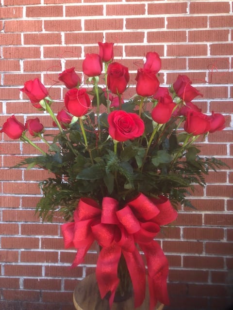 Twenty-four vibrant red roses arranged with greens and a large red bow