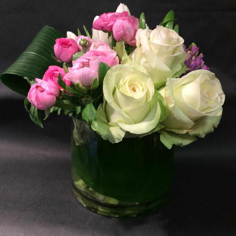 A cluster arrangement of ranuculus, roses and tulips gently embraced by aspidistra