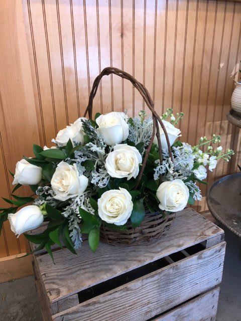 A shorter all around basket arrangement that includes white roses, dusty miller