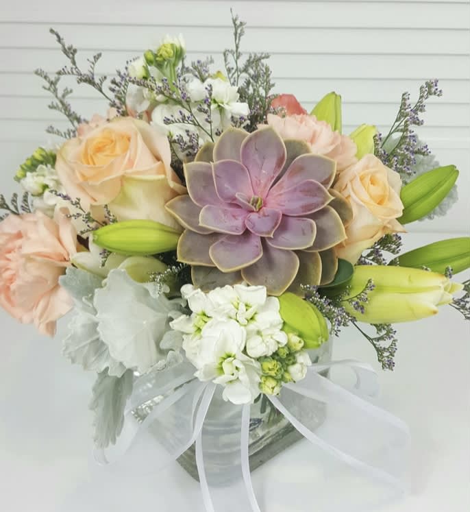 White lilies, roses, stocks, succulent and fillers in a clear rectangular vase
