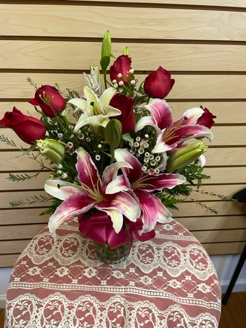 Mixed arrangement with red roses, stargazer lilies, and wax flowers in a