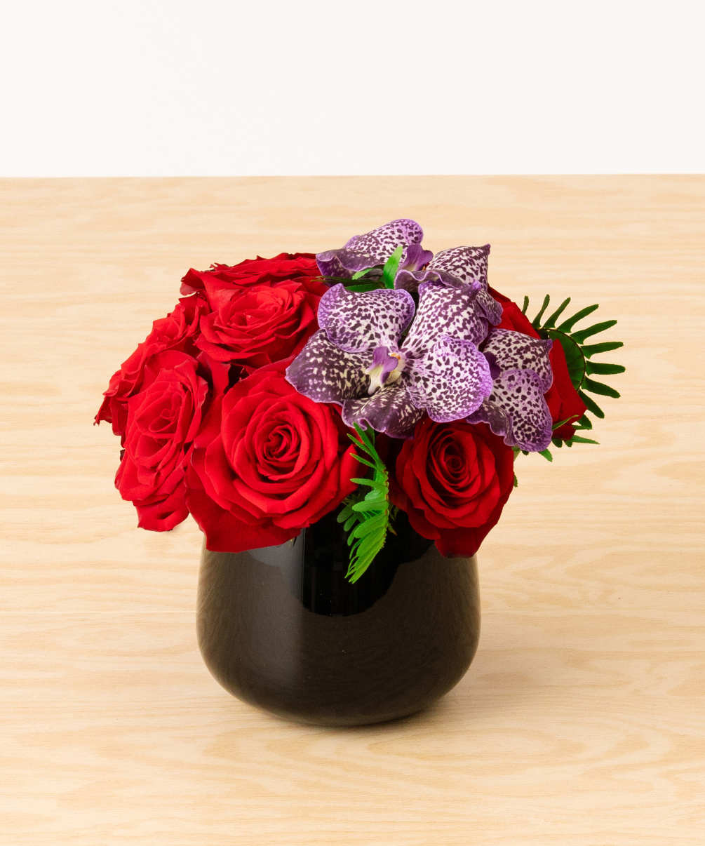 A lush mound of red roses boast purple vanda orchids designed in