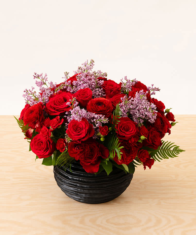 Fragrant lilac peeking through luxurious red roses, spray roses, and ranunculus designed