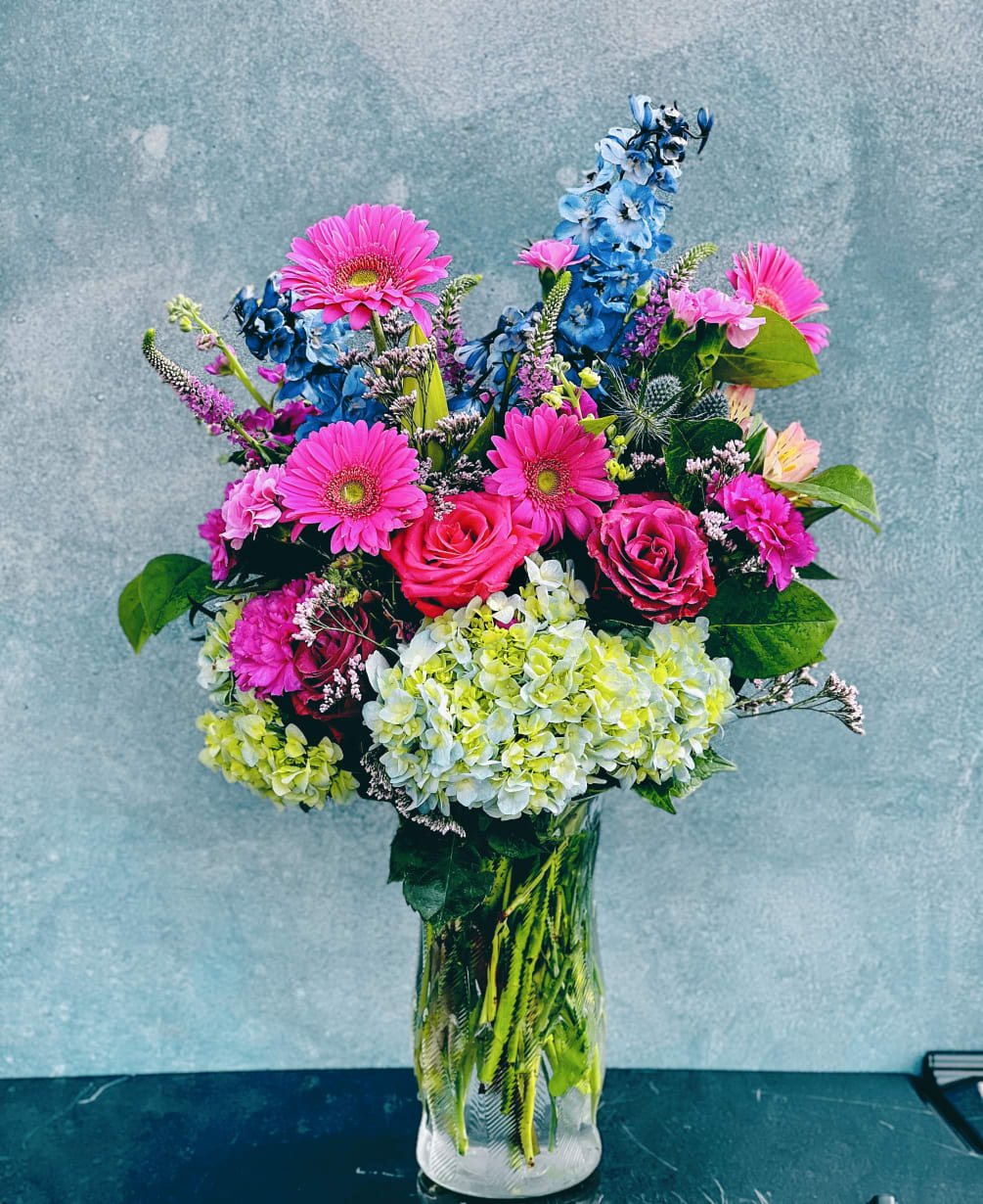 Colorful blooms designed in heighten vase. 

Hydrangeas, Gerber daises, roses , delphiniums