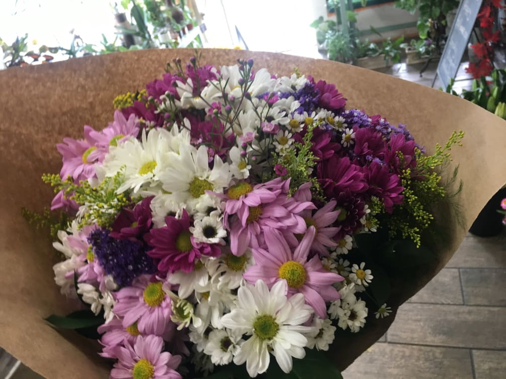 A hand tied bouquet, Mixed colorful daisies with seasonal fillers and foliage