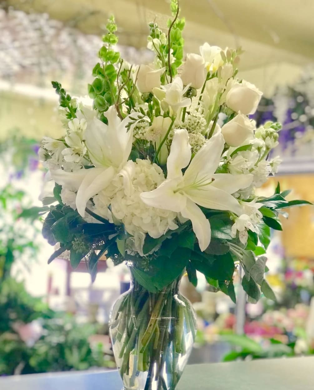 An all white arrangement with premium flowers in a clear glass vase