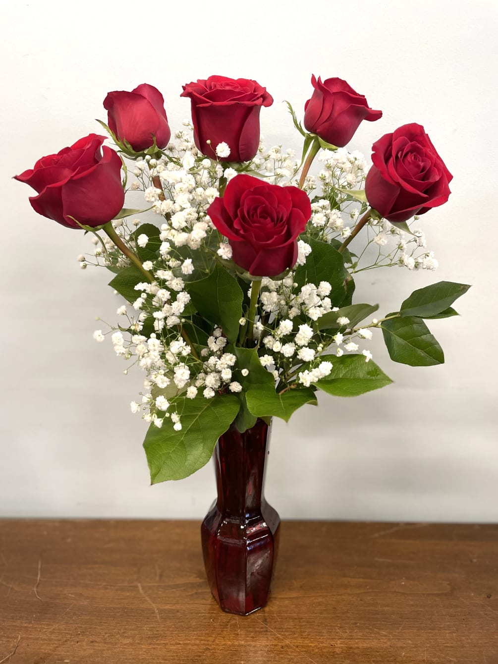 6 red roses are arranged in a red glass vase with babies