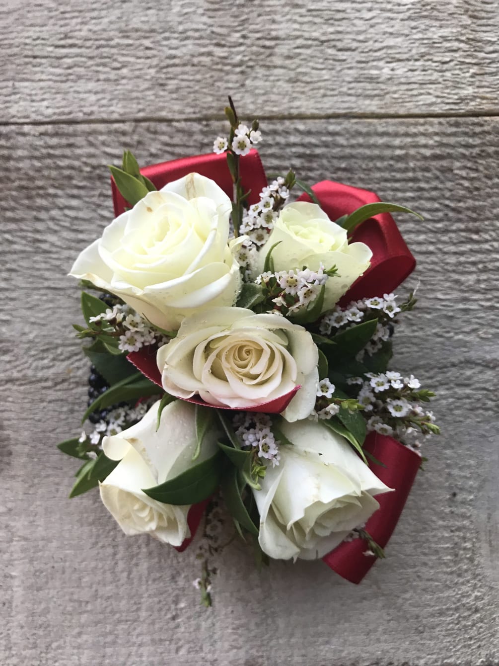 White Spray roses, greenery, filler with Red ribbon on pearl wristband. Greenery