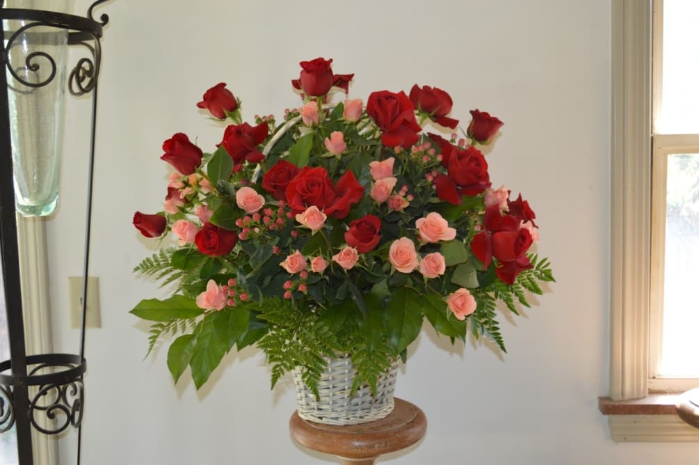 Pink spray roses and red roses arranged in a white wicker basket