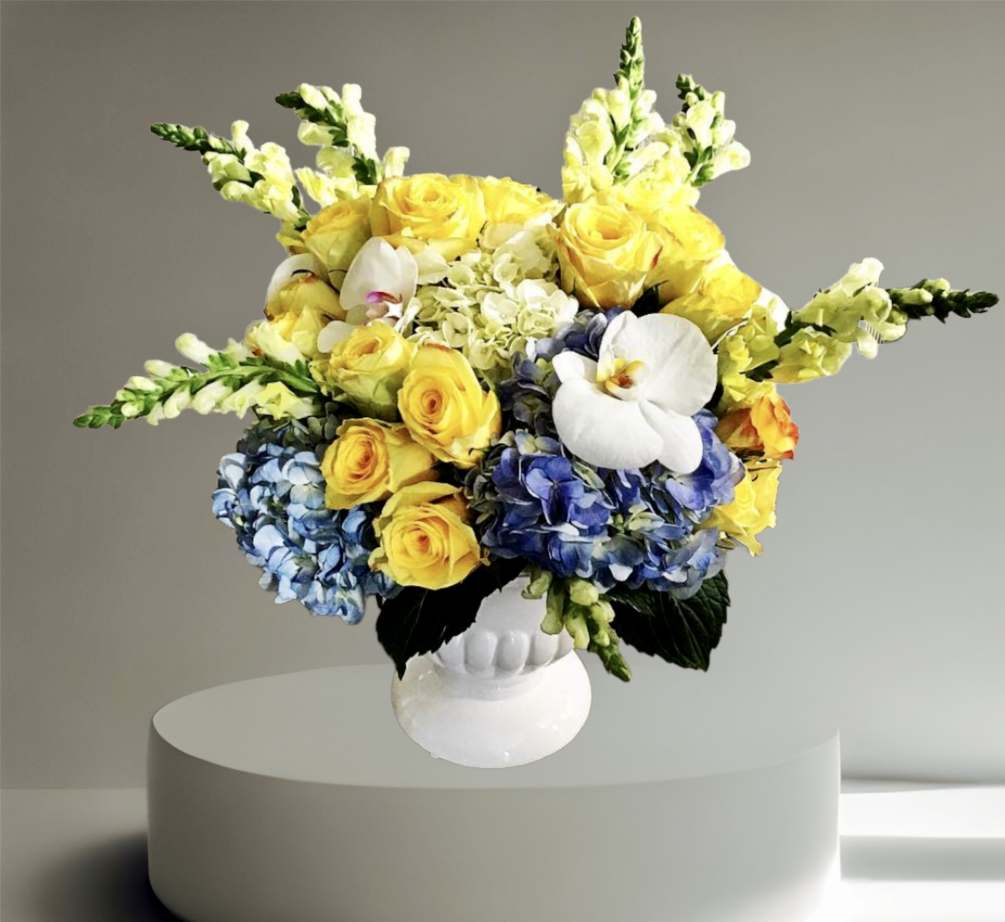 A grand arrangement with blue hydrangea, yellow roses, orchids, and snapdragon arranged