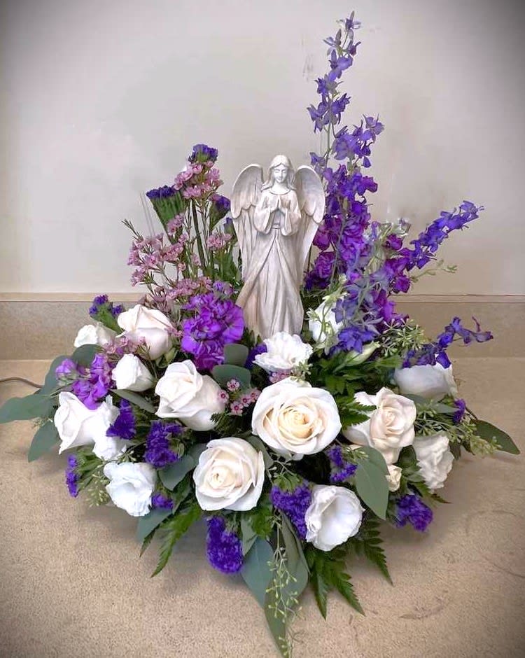 White and purple arrangement which includes an angel statue. If statue is