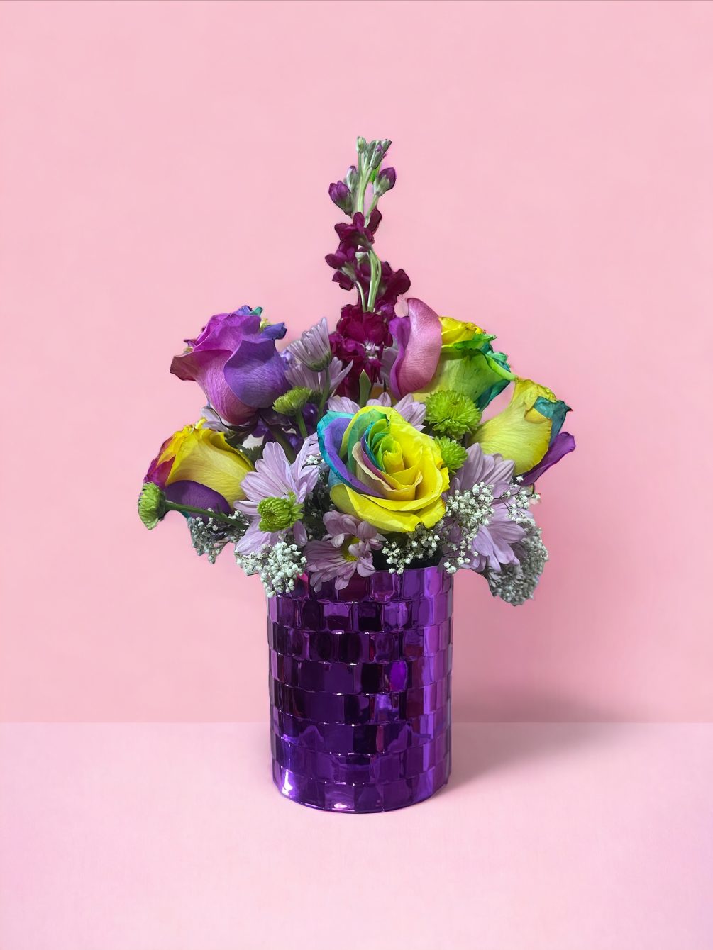 A colorful arrangement made of rainbow roses, pompons, stock and baby&#039;s breath.
