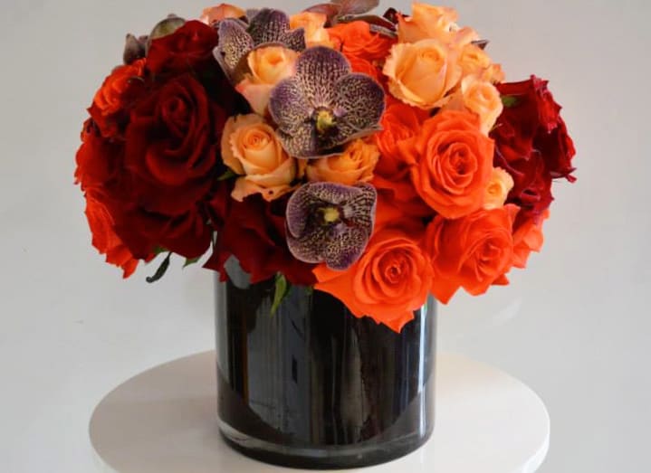Deep orange and red roses, accented by rust-colored cymbidium orchids in a