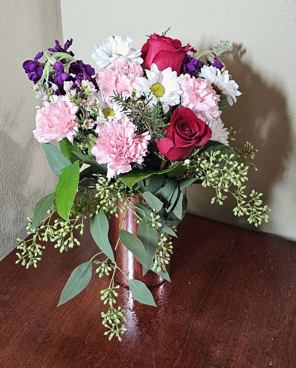 Pink reflective vase with assortment of pink, white, and purple flowers.