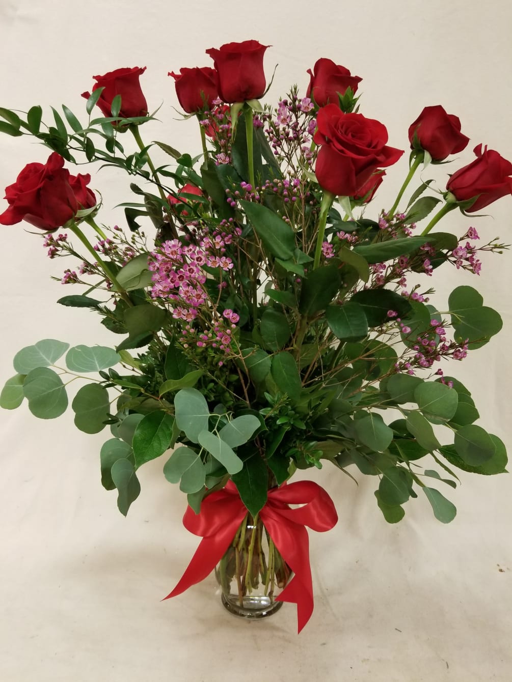 Twelve perfect roses, arranged in a clear glass vase. Premium foliage and