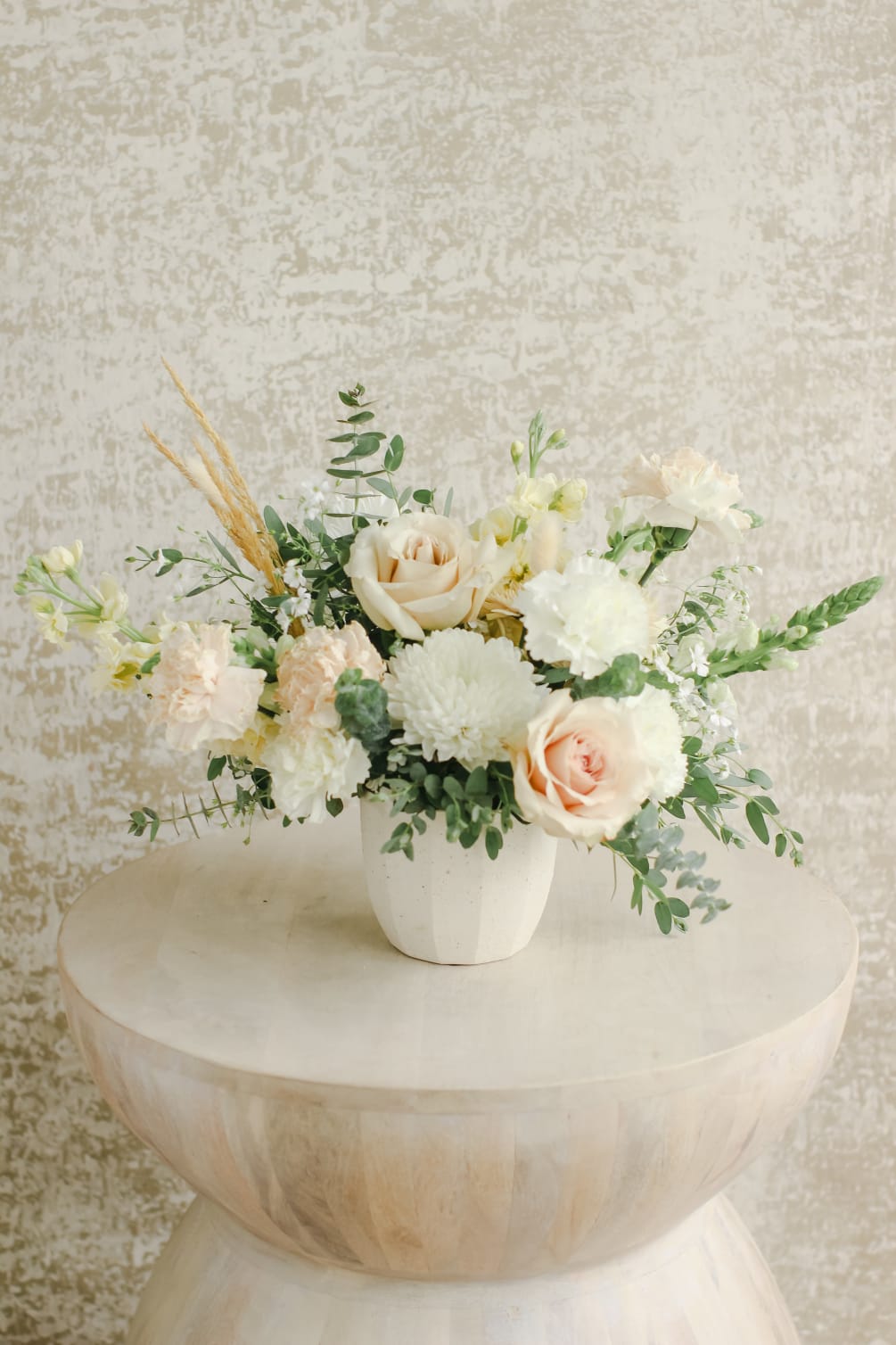 A delicate arrangement including soft champagne colored blooms and textural elements. Designed
