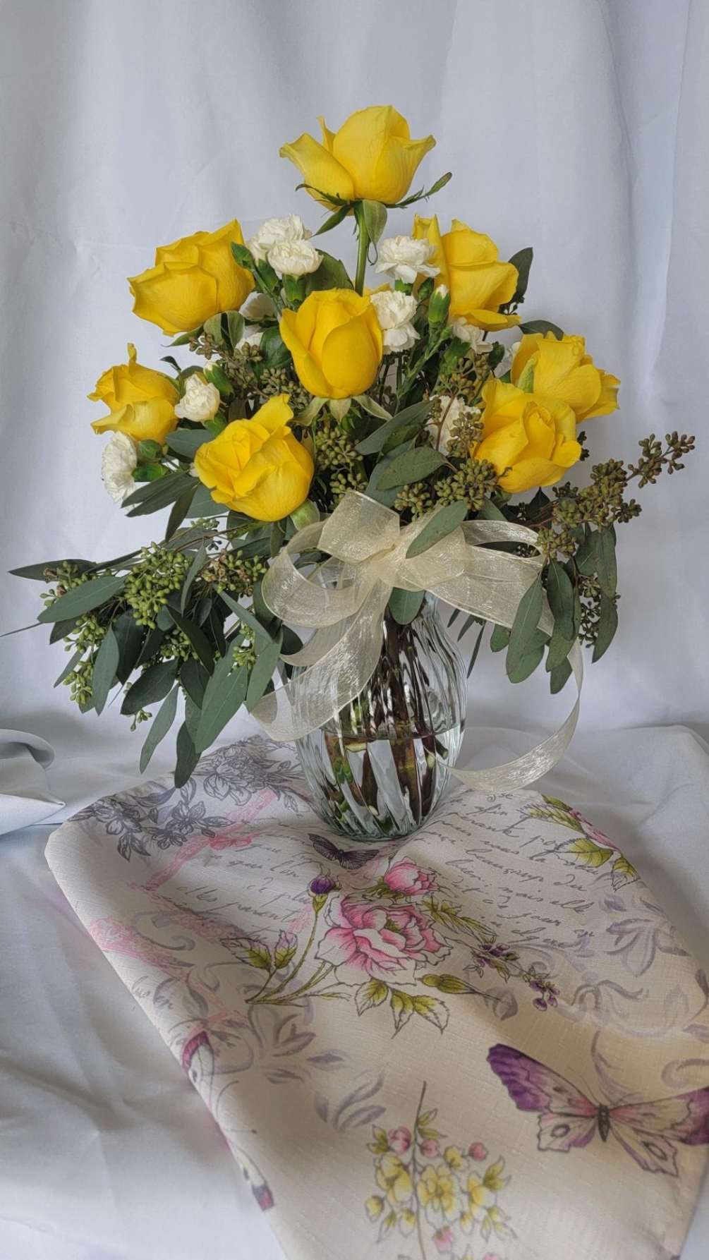 8 yellow roses and white carnations surrounded by seed eucalyptus n a