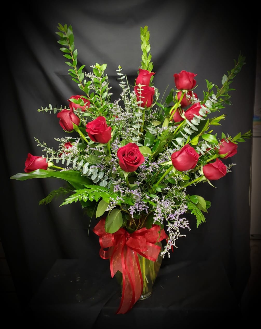 18 Long stem red roses fill with various select greens and limonium.