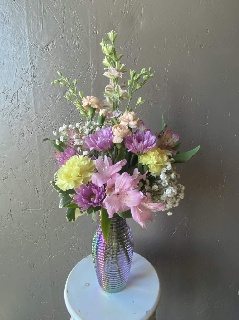 Pastel mixed florals fill a beautiful lavender iridescent vase. All flowers and