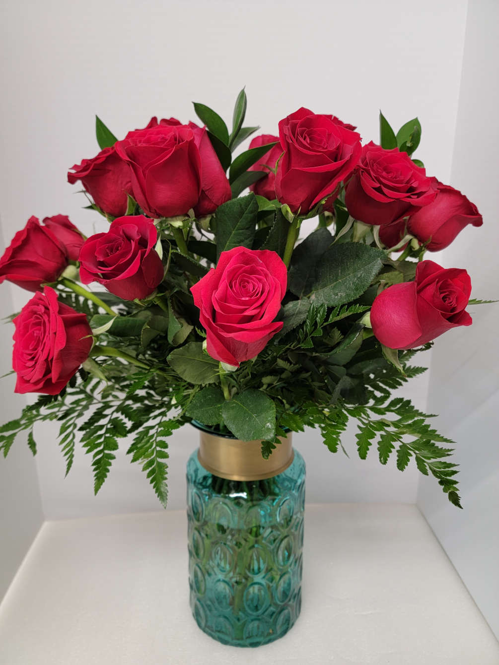 Twelve red roses and greens in a very elegant aqua vase.