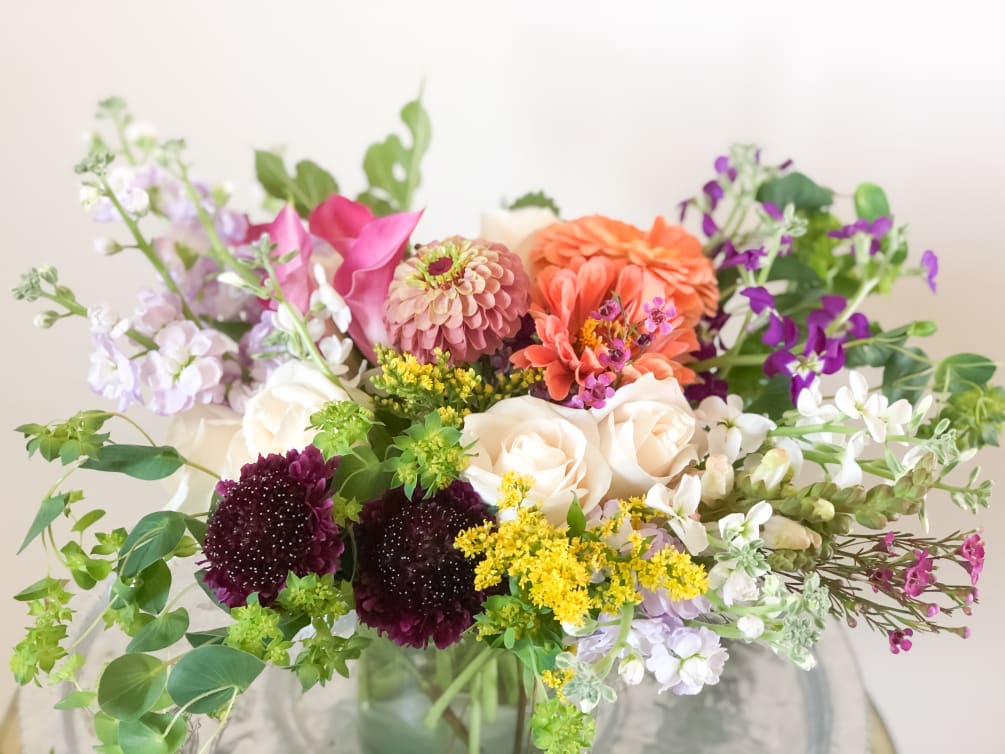 Lavender, purple, peach and white blooms with seasonal foliage in a glass
