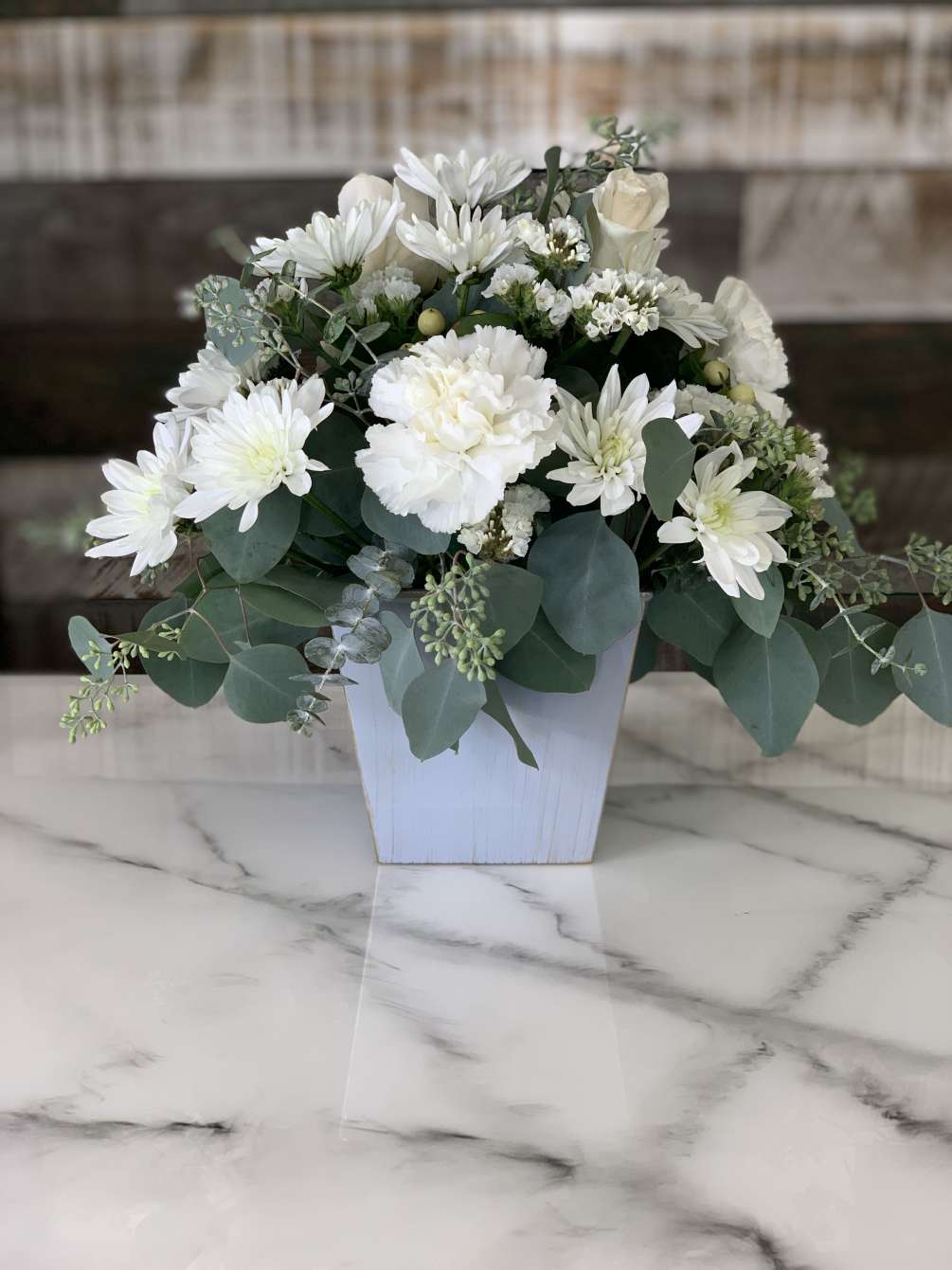 All white roses, carnations, hypericum berries, and mums with assorted greenery.