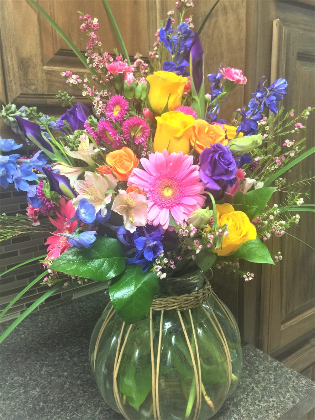 Bright colorful arrangement with roses. gerberas ,iris ,delp  astro 
container may