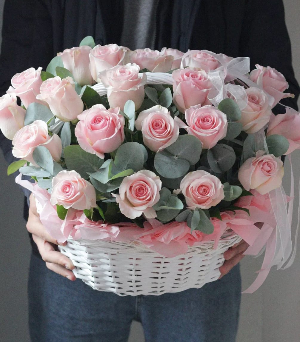 A basket filled with two dozen of pink roses with greens. 