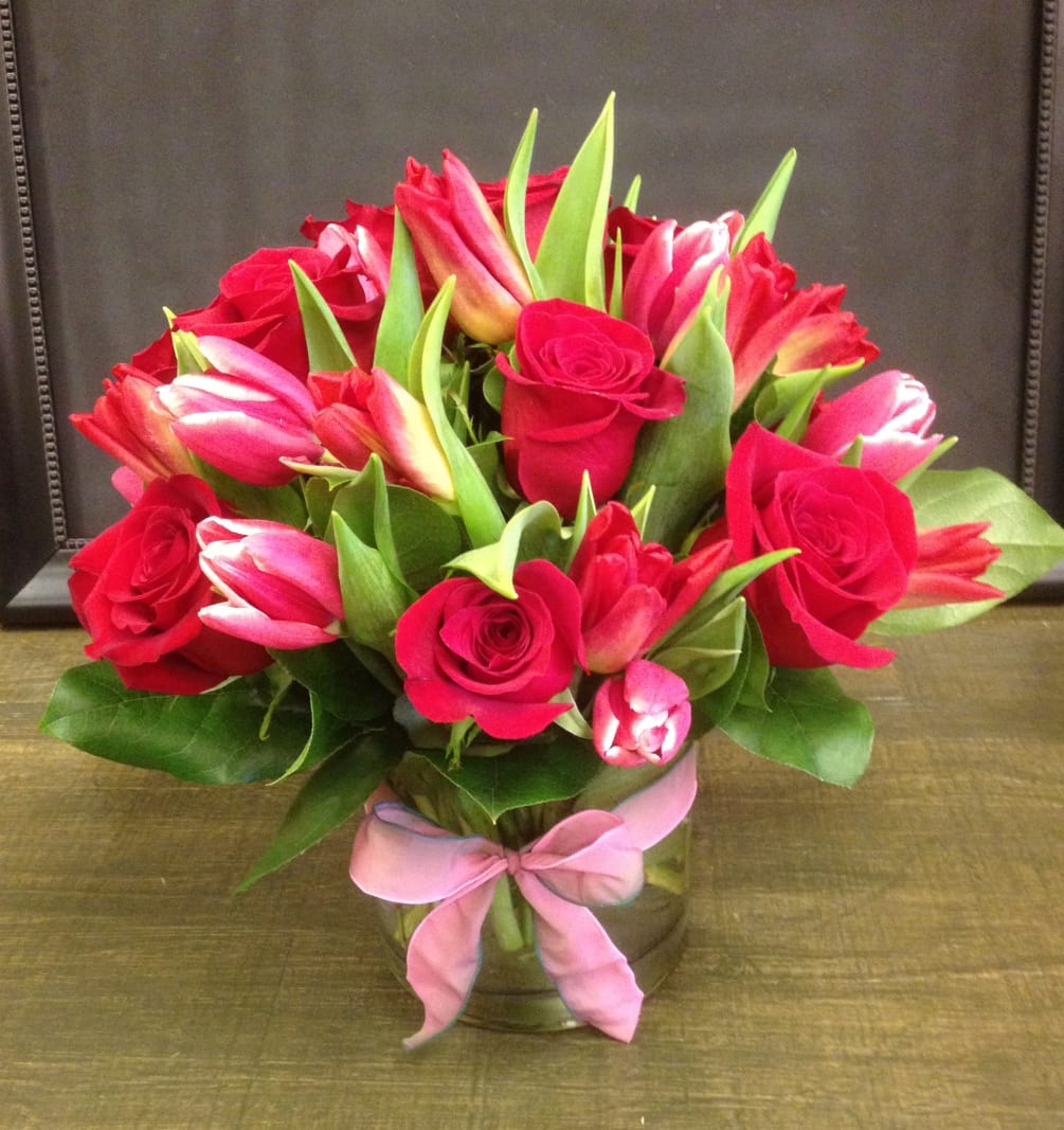 One dozen red roses, tulips and lemon leaf fill a glass cylinder.